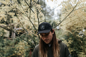Model in SKELE-MOON desing embroidered onto a black DAD CAP - doomsdayco SKELE-MOON DAD CAP forestry background